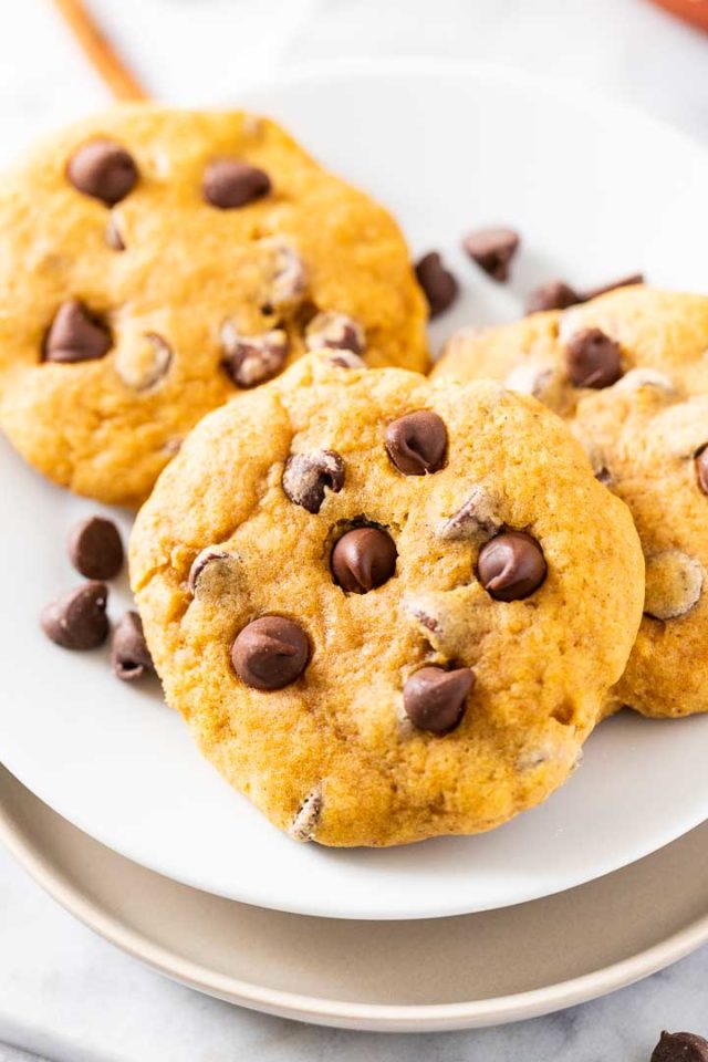 Close-up of 3 chocolate chip cookies on a white plate with chocolate chips.