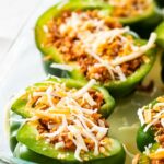 A glass baking dish with halved green peppers stuffed with ground turkey and topped shredded cheese.