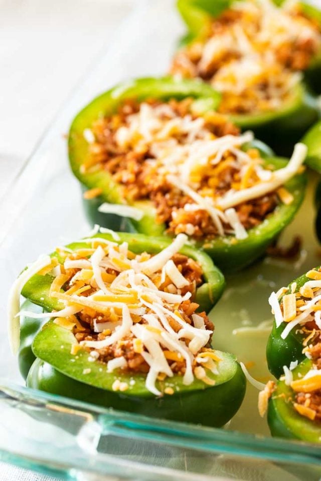 A glass baking dish with halved green peppers stuffed with ground turkey and topped shredded cheese.
