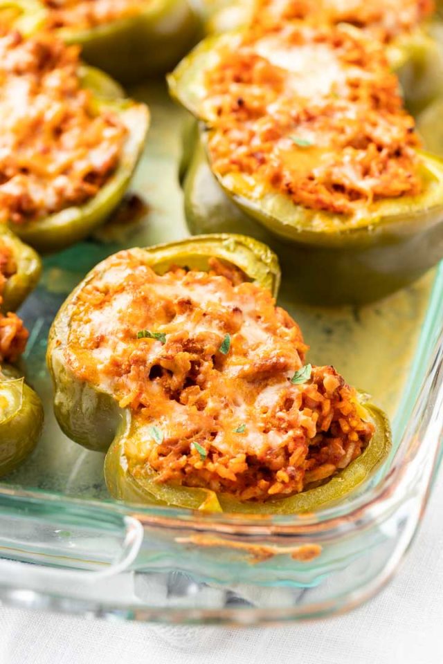 Glass baking dish with baked stuffed green peppers garnished with parsley.
