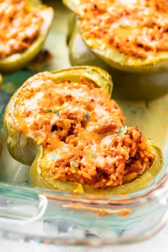 Close-up of glass baking dish with baked stuffed green peppers garnished with parsley.