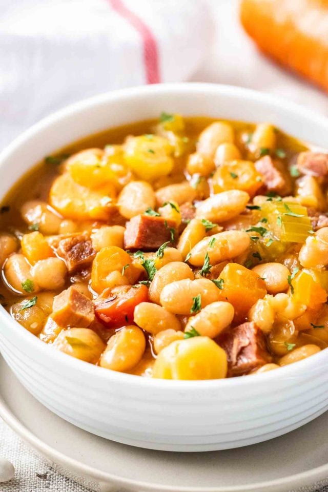 A white bowl containing ham and white bean soup, garnished with parsley.