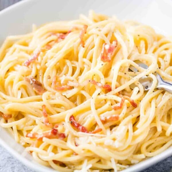 Spaghetti Carbonara on a white plate with a fork in it.