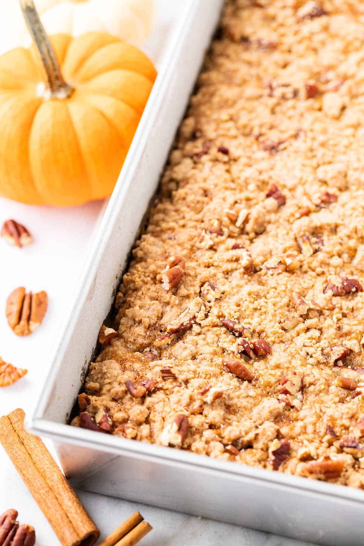 A baking pan, with pumpkin crunch cake with pecans and whole pecans and a pumpkin next to it.