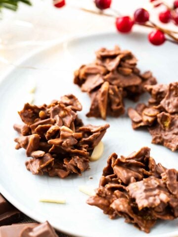 chocolate covered clusters of corn flakes and almonds on a grey plate, garnished with almonds and cranberries