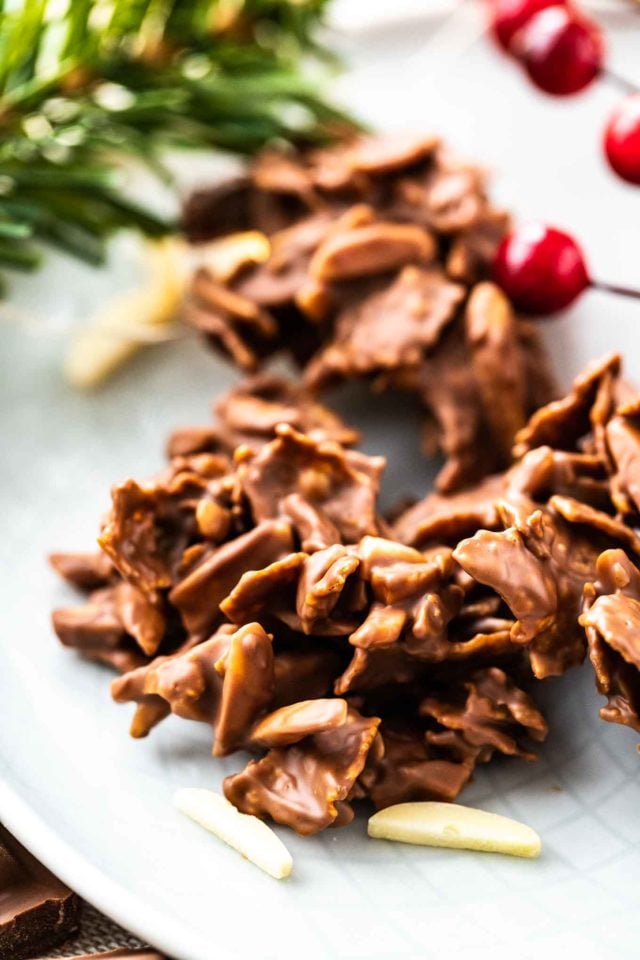 Close-up of chocolate covered clusters of corn flakes and almonds on a grey plate, garnished with almonds and cranberries