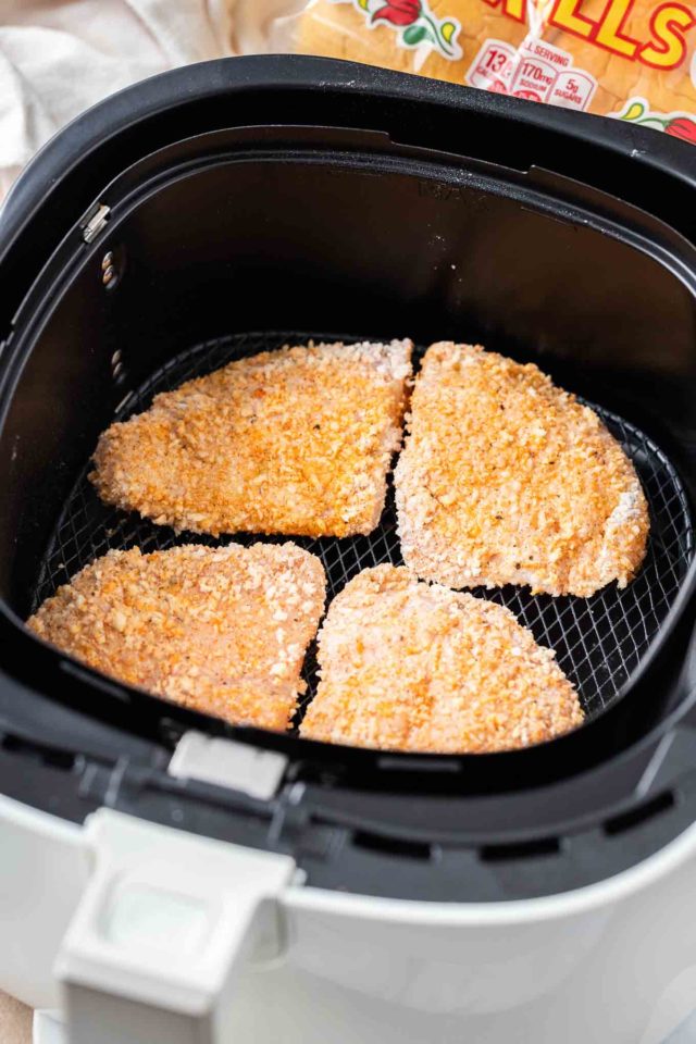Four breaded chicken breasts in an air fryer basket.