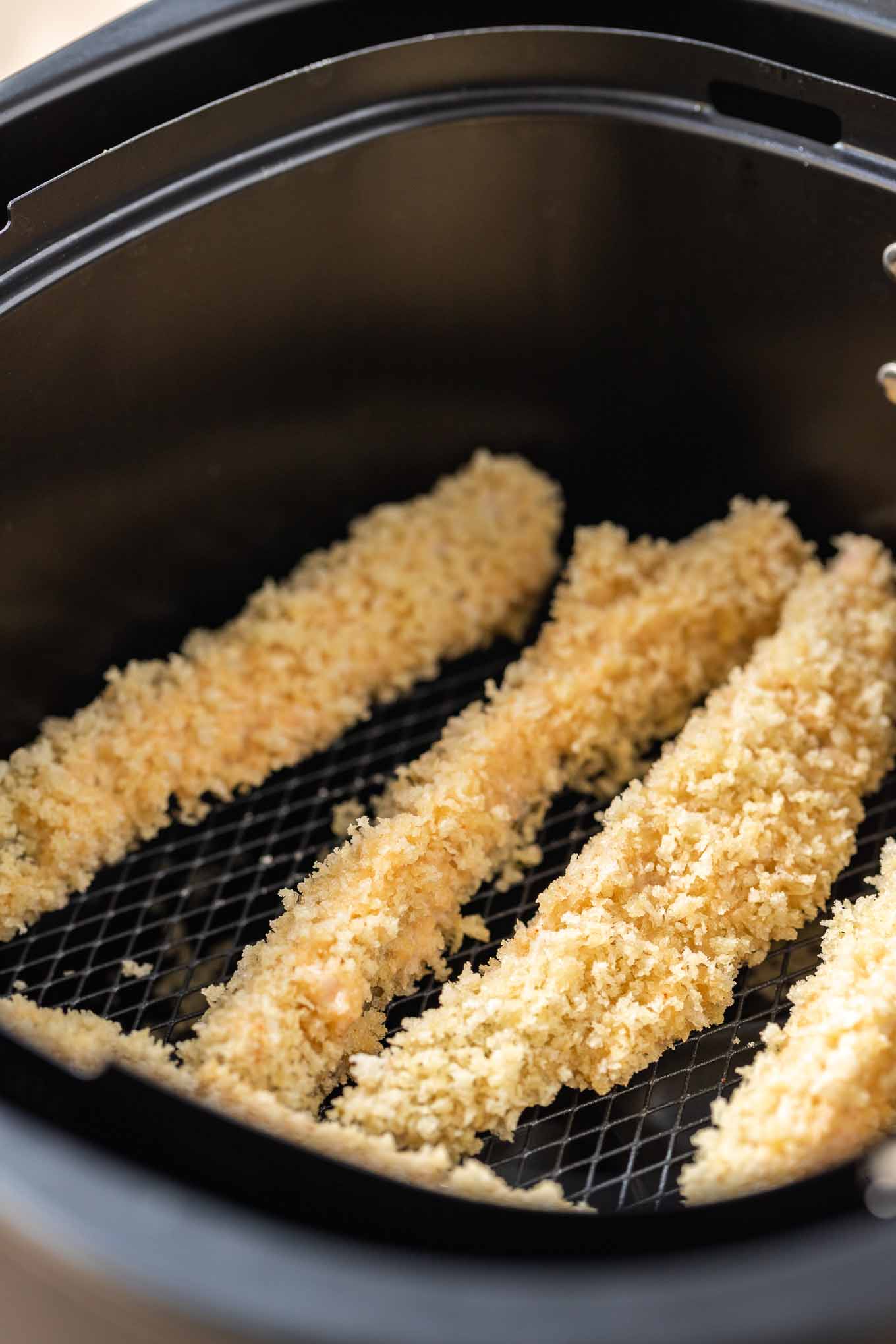 Breaded pickle spears in an air fryer basket.