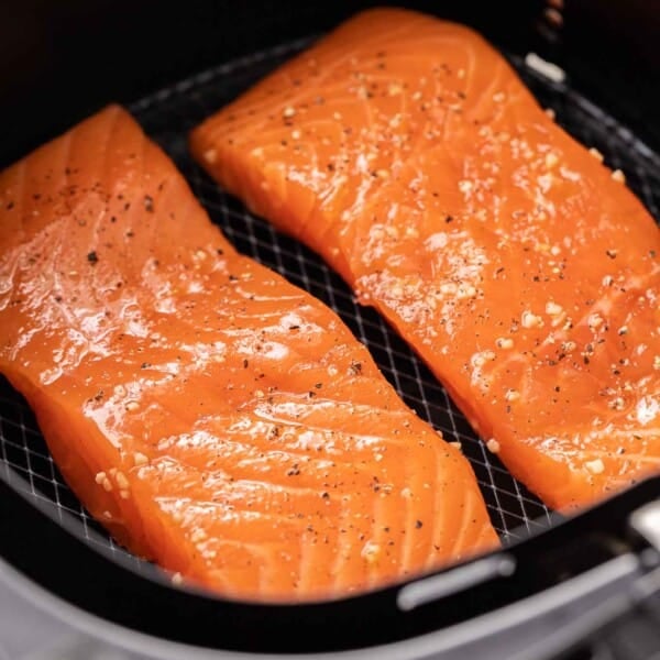 Two pieces of salmon, seasoned with salt and pepper in an airfryer basket