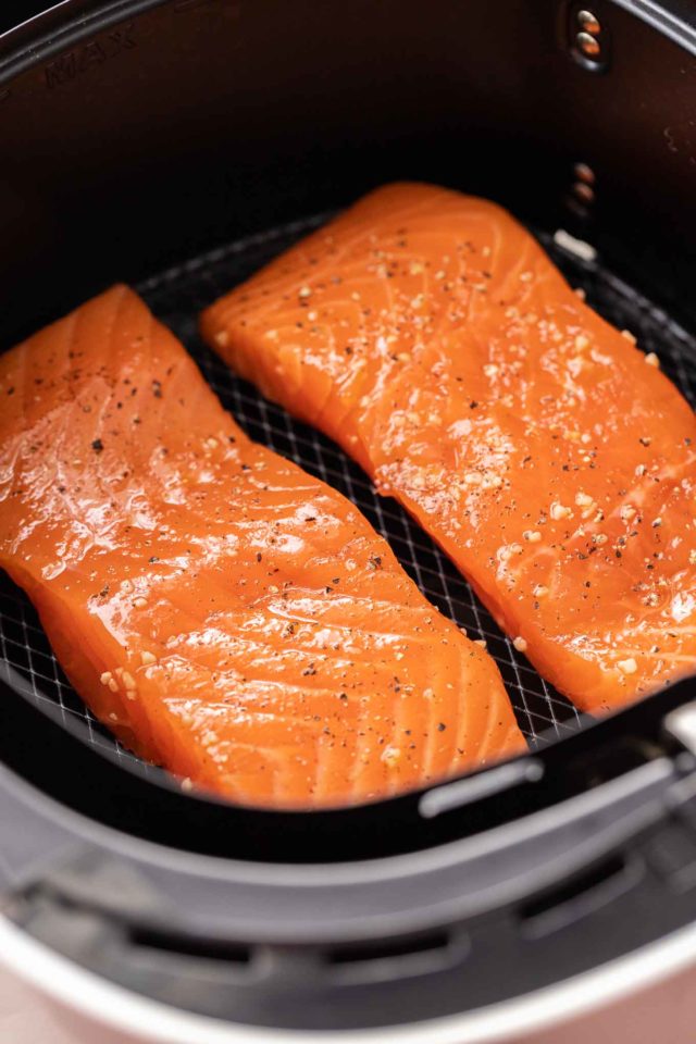 Two pieces of salmon, seasoned with salt and pepper in an airfryer basket