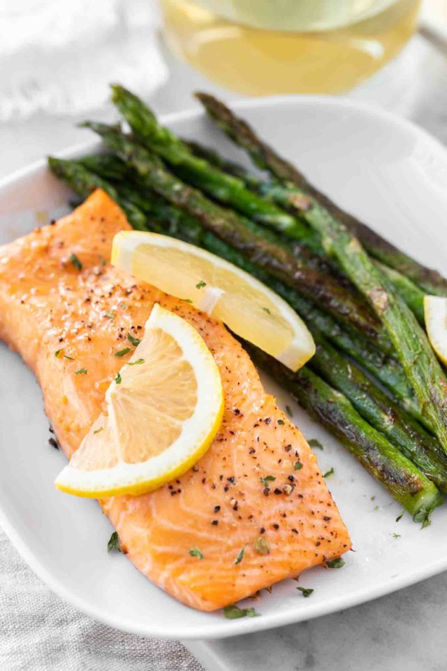 a piece of salmon on a white plate next to some roasted asparagus and garnished with lemon slices