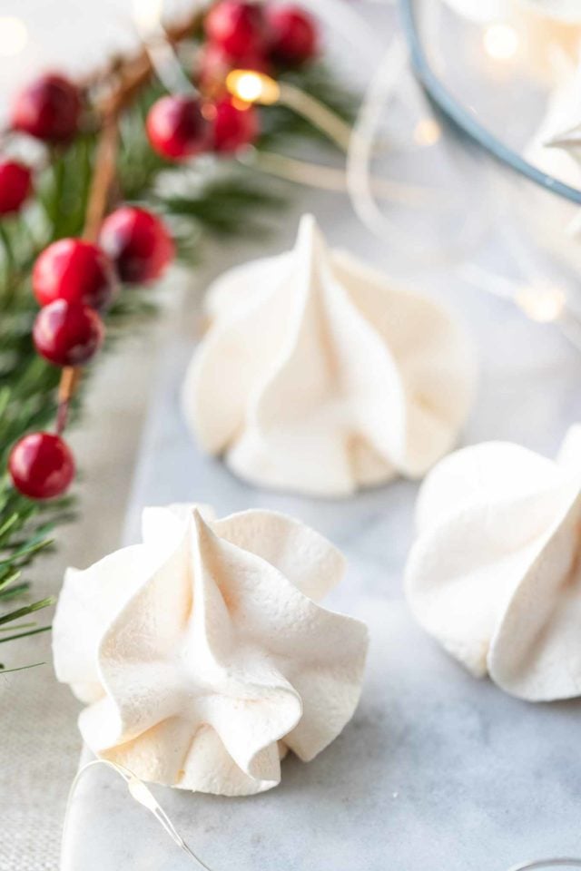Three meringue cookies sitting on a grey surface with some Cranberries