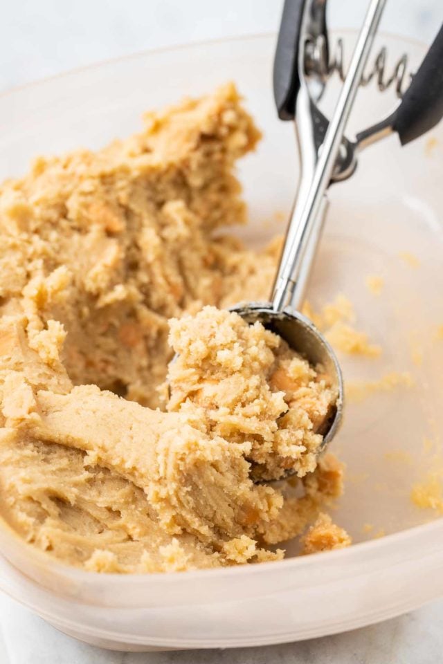 butterscotch cookie dough in a glass bowl being scooped up with a cookie scoop