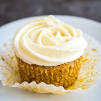 A carrot cupcake with frosting on a white plate.