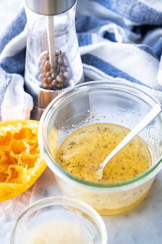 salad dressing in a glass bowl with a spoon in it with a squeezed orange and a pepper mill in the background