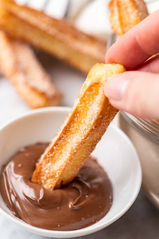 sugared churro being dipped into nutella, churros in the background