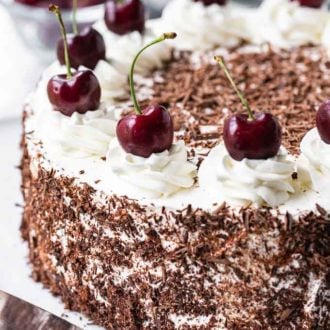 Black Forest Cake. The cake has chocolate shavings on the side and swirls of whipped cream topped with whole cherries on top