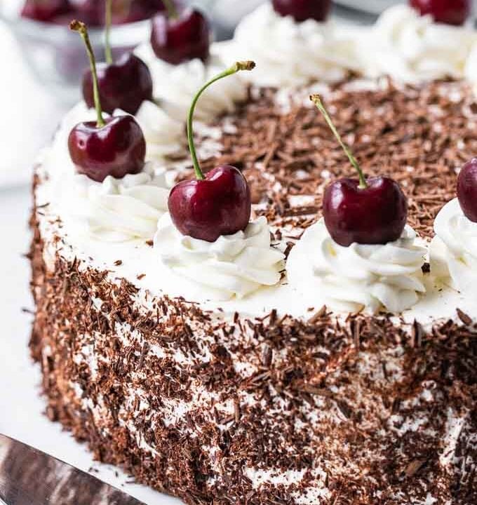 Black Forest Cake. The cake has chocolate shavings on the side and swirls of whipped cream topped with whole cherries on top
