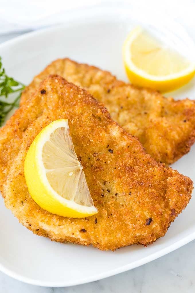 Two fried Schnitzels on a white plate, garnished with a wedge of lemon and parsley