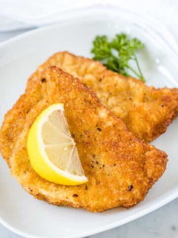 Two fried Schnitzels on a white plate, garnished with a wedge of lemon and parsley