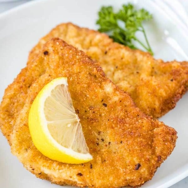 Two fried Schnitzels on a white plate, garnished with a wedge of lemon and parsley