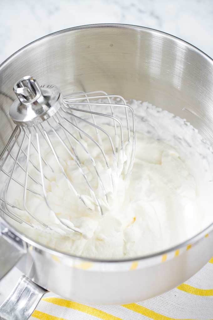 Whipped Cream in a stainless steel bowl, with a Kitchen Aid whisk