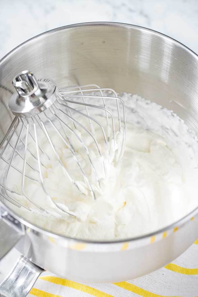 Whipped cream in a stainless-steel bowl, with a Kitchen Aid whisk.