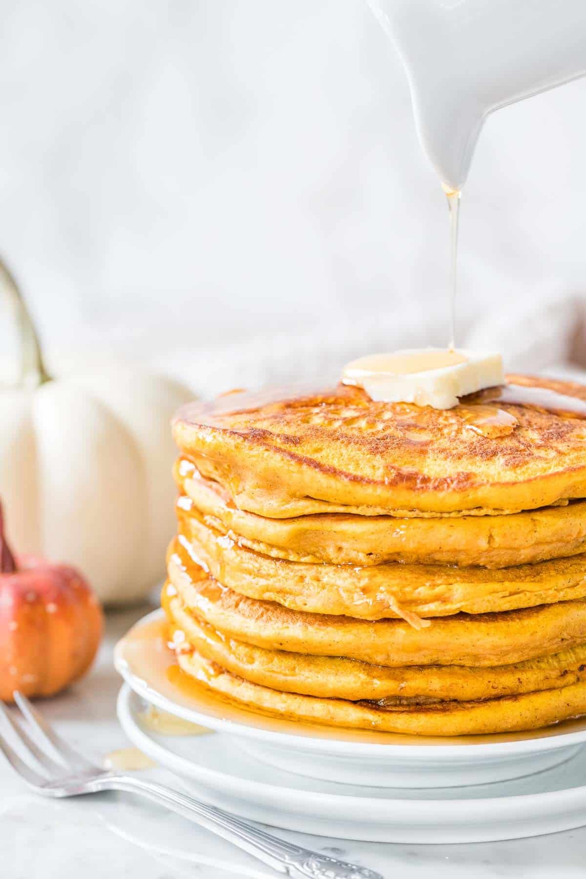 A stack of Pumpkin Pancakes topped with butter and Maple Syrup drizzled on top.