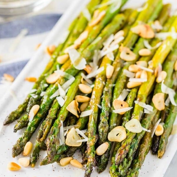 Roasted asparagus on a serving platter, topped with roasted garlic, Parmigiano and pine nuts