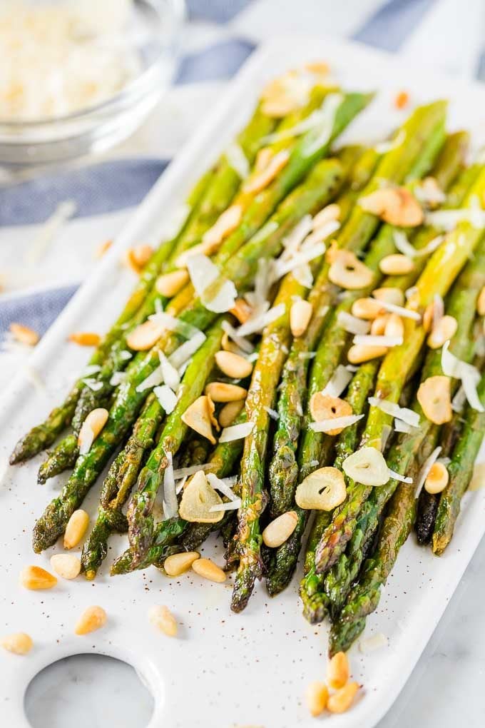 Roasted asparagus on a serving platter, topped with roasted garlic, Parmigiano and pine nuts