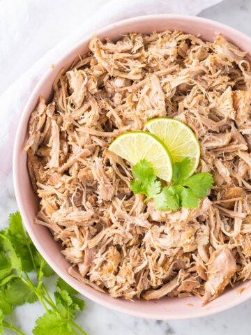 Slow Cooker Carnitas in a pink bowl garnished with lime wedges and cilantro