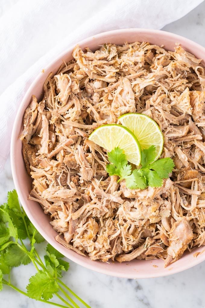 Slow Cooker Carnitas in a pink bowl garnished with lime wedges and cilantro