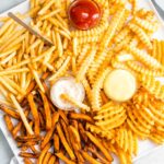 Different french fries on a platter with condiments