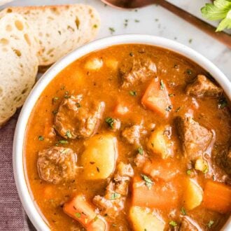 A bowl of beef stew with a spoon and bread next to it
