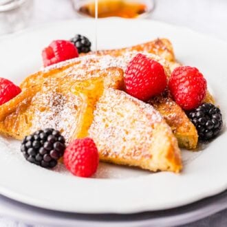 French Toast drizzled with maple syrup on a white plate.