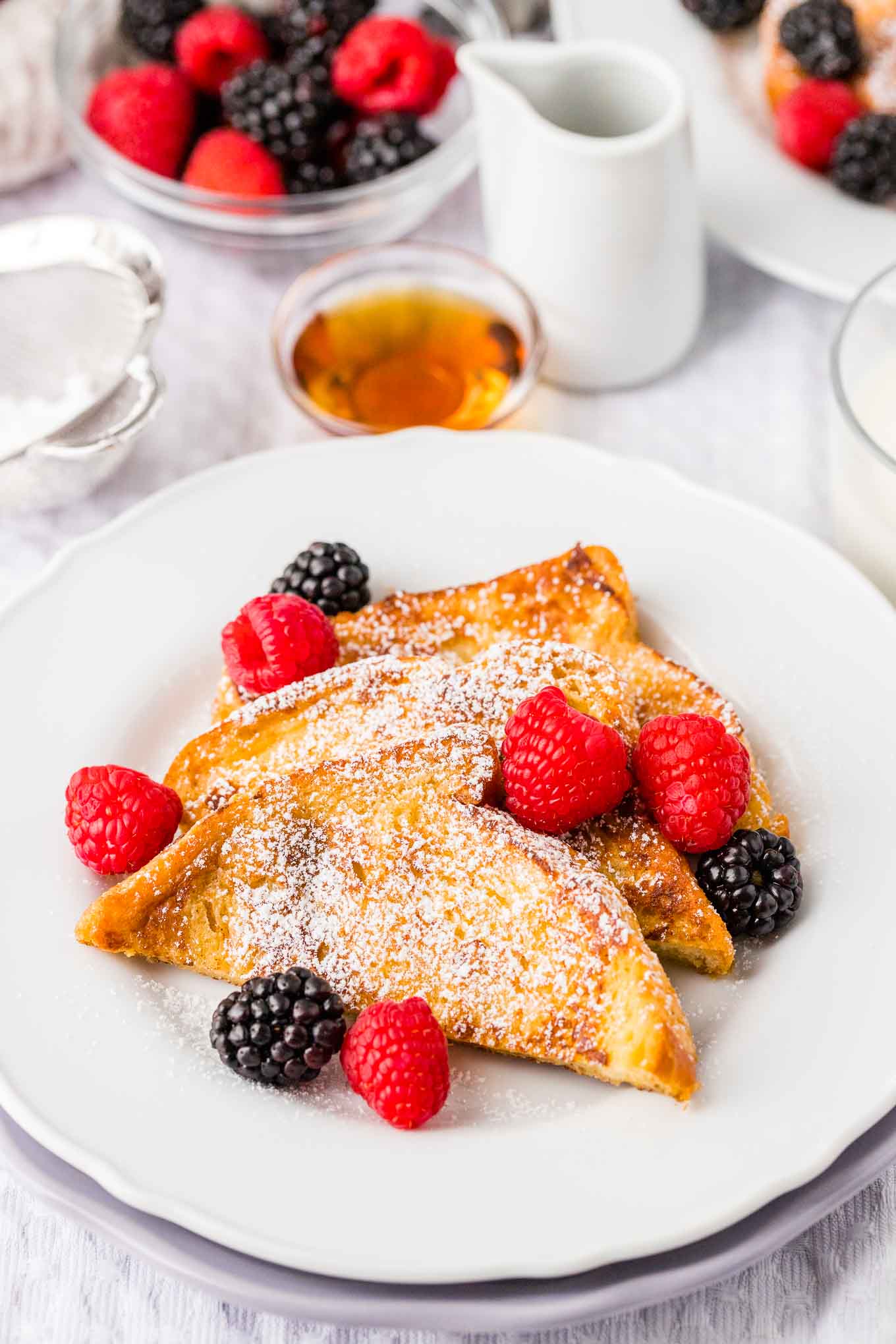 French toast garnished with powdered sugar and berries on a white plate.