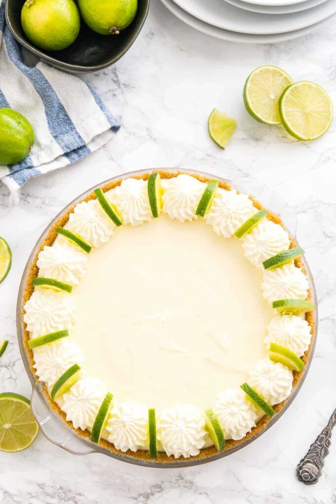 A key lime pie decorated with whipped cream and lime slices