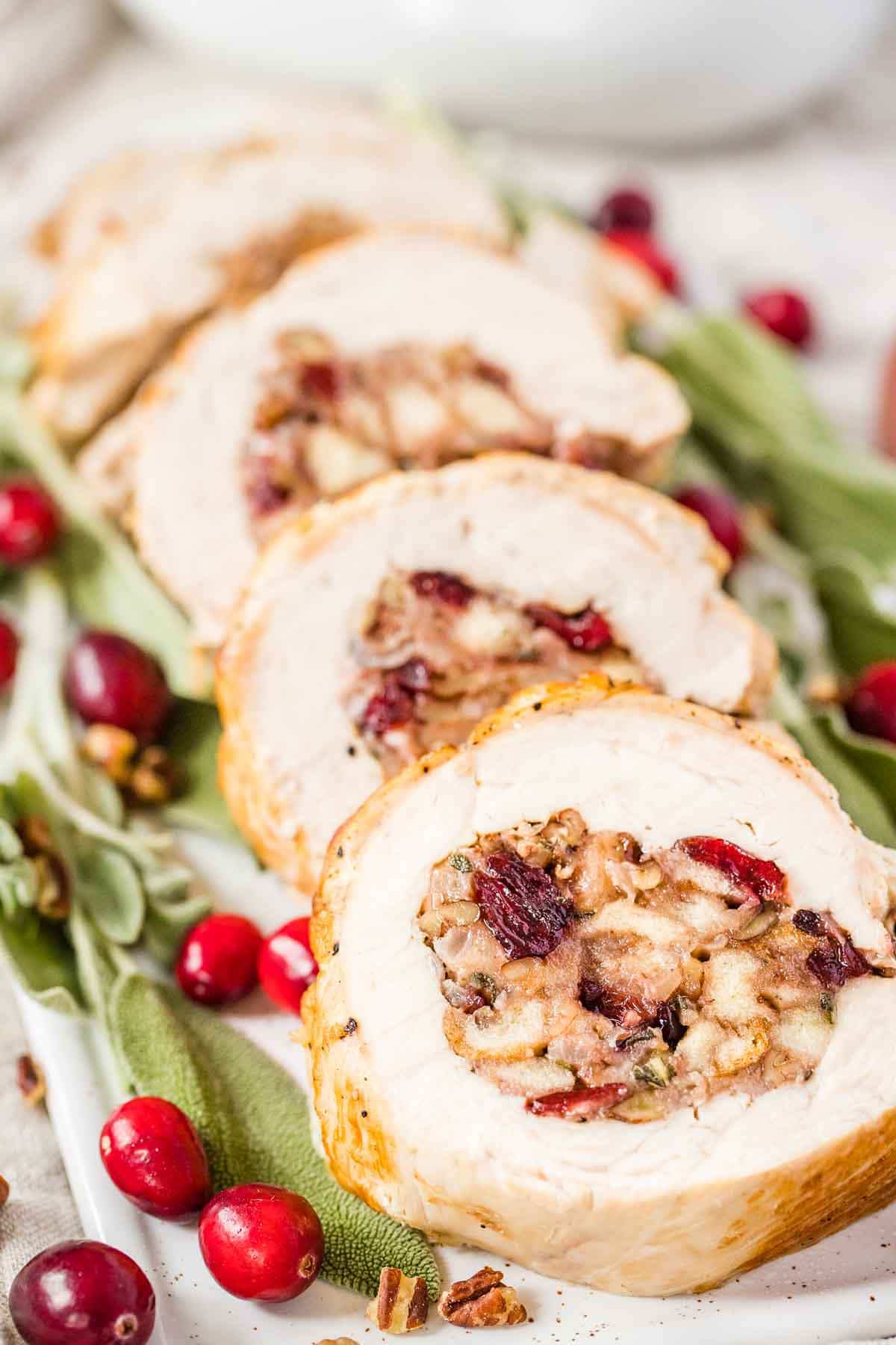 Stuffed turkey breast on a serving plate garnished with cranberries and sage