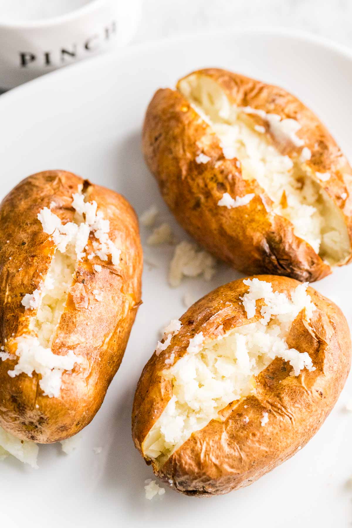 Baked potatoes cut open and fluffed with a fork on a white plate