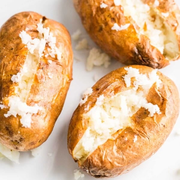 Baked potatoes cut open and fluffed with a fork on a white plate