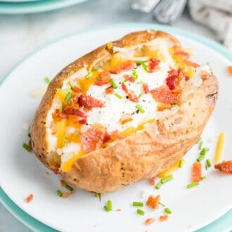 An air fried baked potato garnished with sour cream, bacon, and cheese on a white plate