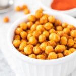 Air fried chickpeas in a white bowl next to a bowl of spices