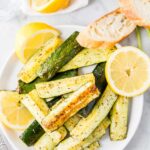 Roasted Zucchini on a white plate garnished with lemon slices