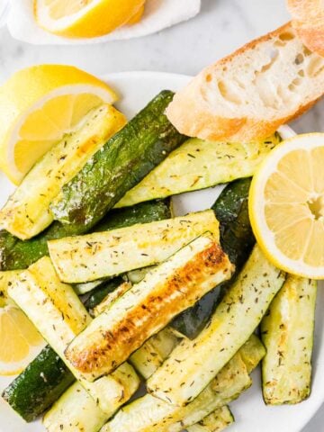 Roasted Zucchini on a white plate garnished with lemon slices