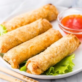 Egg Rolls on a white plate next to a bowl of sauce