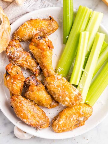 A white plate with crispy chicken wings next to celery stalks.