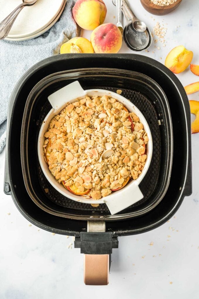 A cooked peach crumble in a baking pan in an air fryer basket