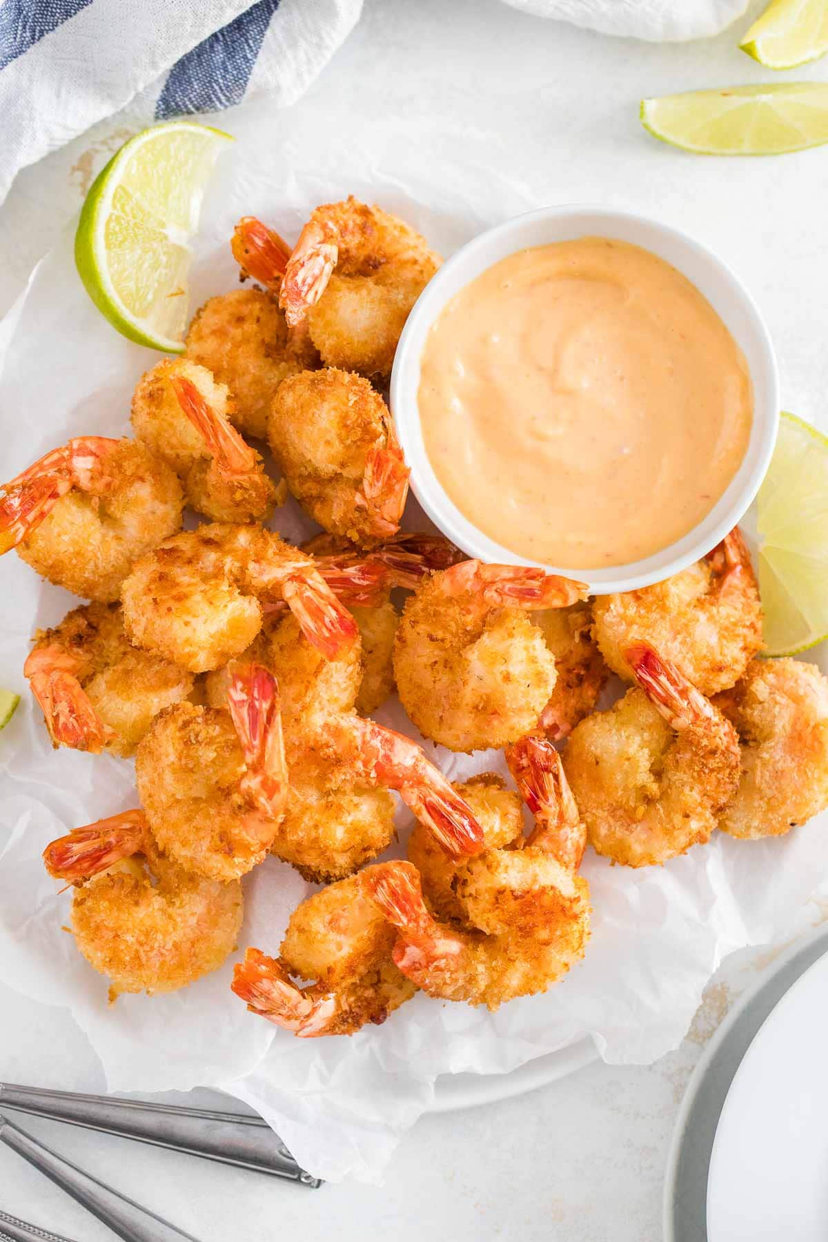 Breaded shrimps on white parchment paper next to a small white bowl of sauce.