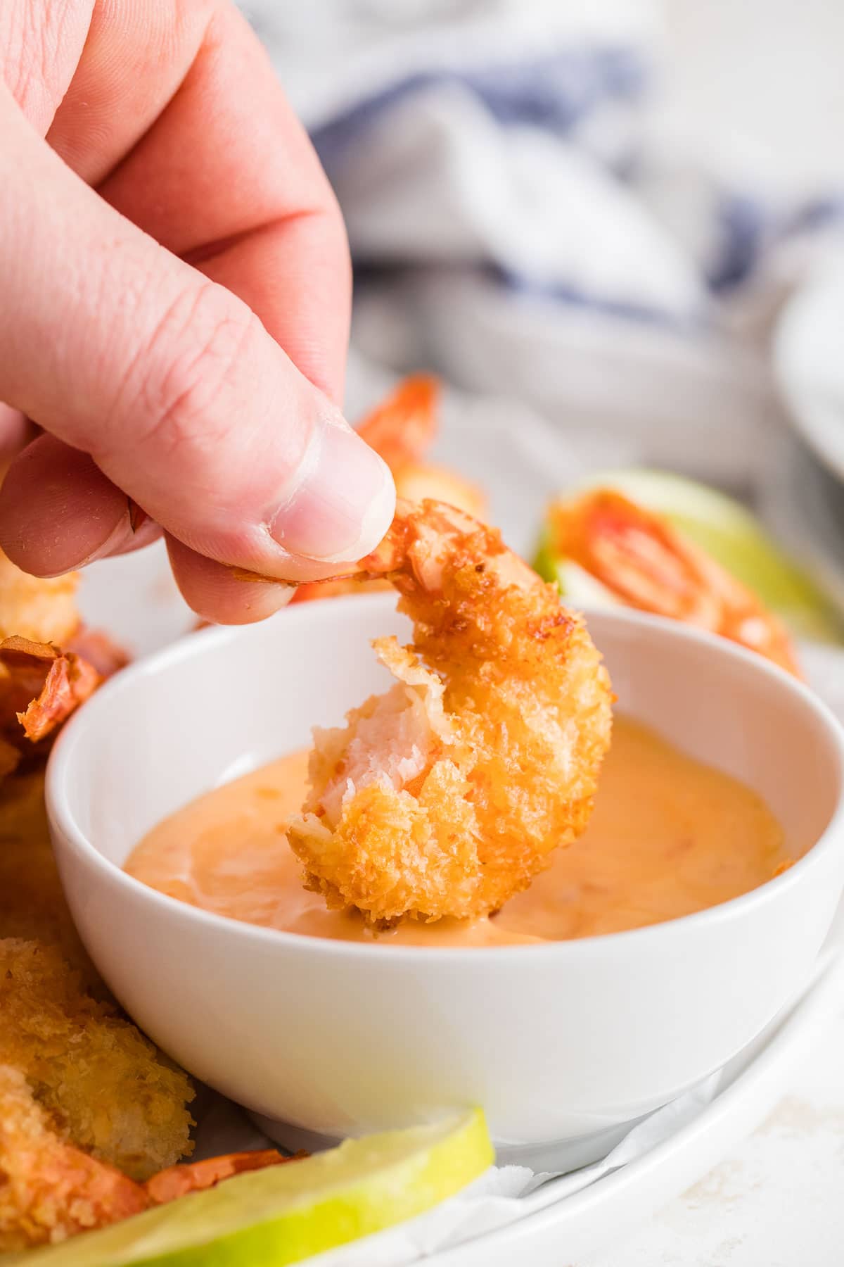 A single breaded shrimp dipped into an orange sauce in a small white bowl.