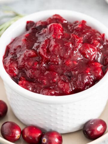 A close up of cranberry sauce in a small bowl garnished with whole cranberries and a spoon next to it.